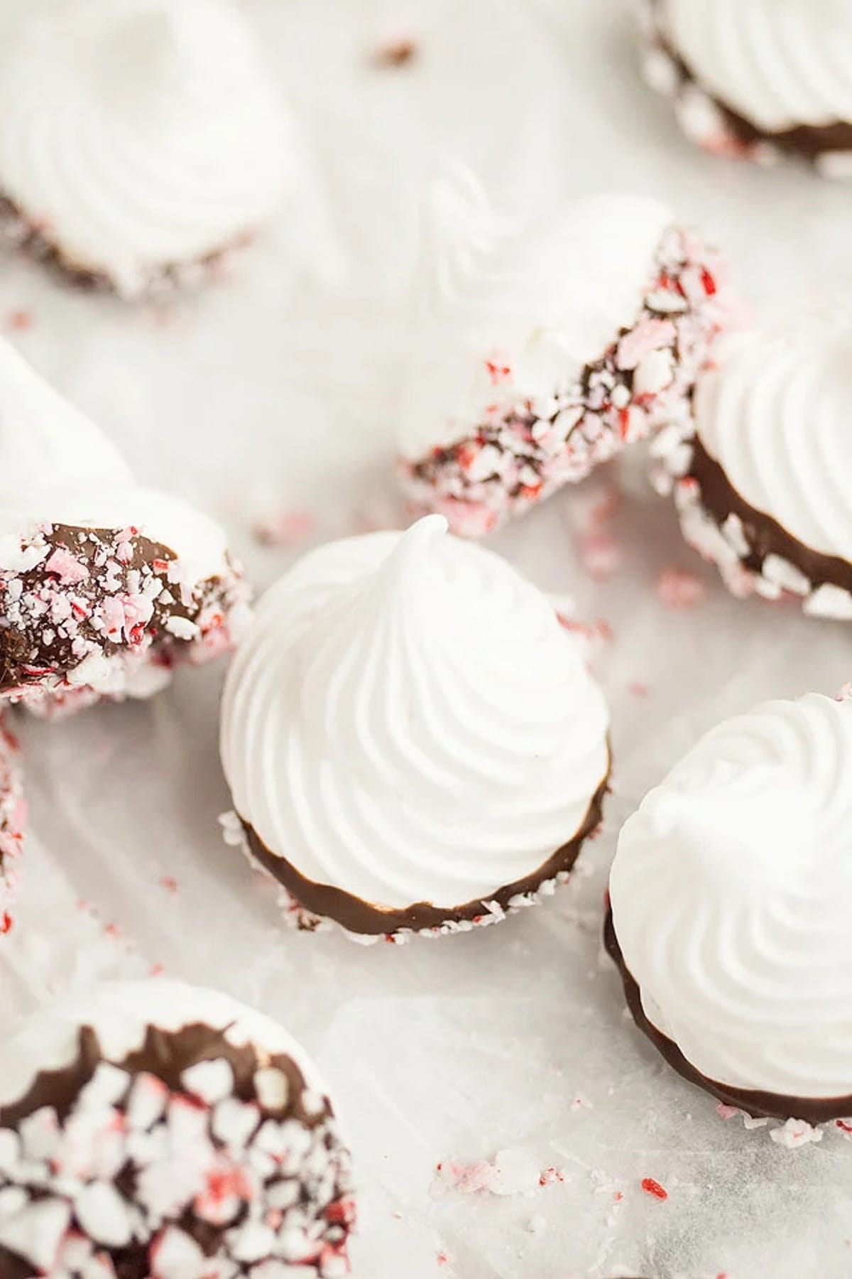 Chocolate dipped meringue kisses scattered on a white surface.