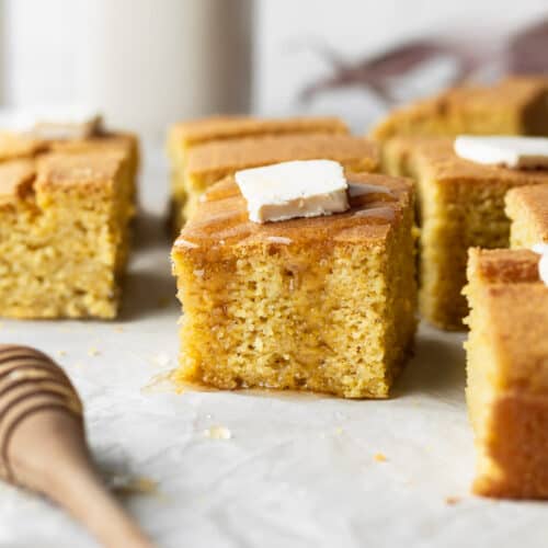A piece of gluten-free cornbread with a pad of butter and drizzle of honey.