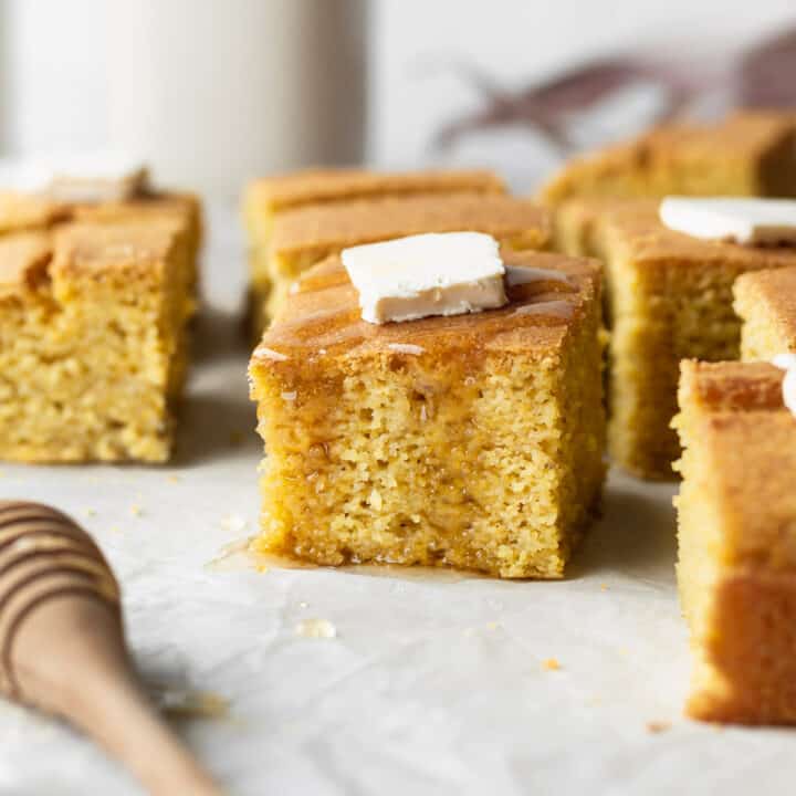 A piece of gluten-free cornbread with a pad of butter and drizzle of honey.