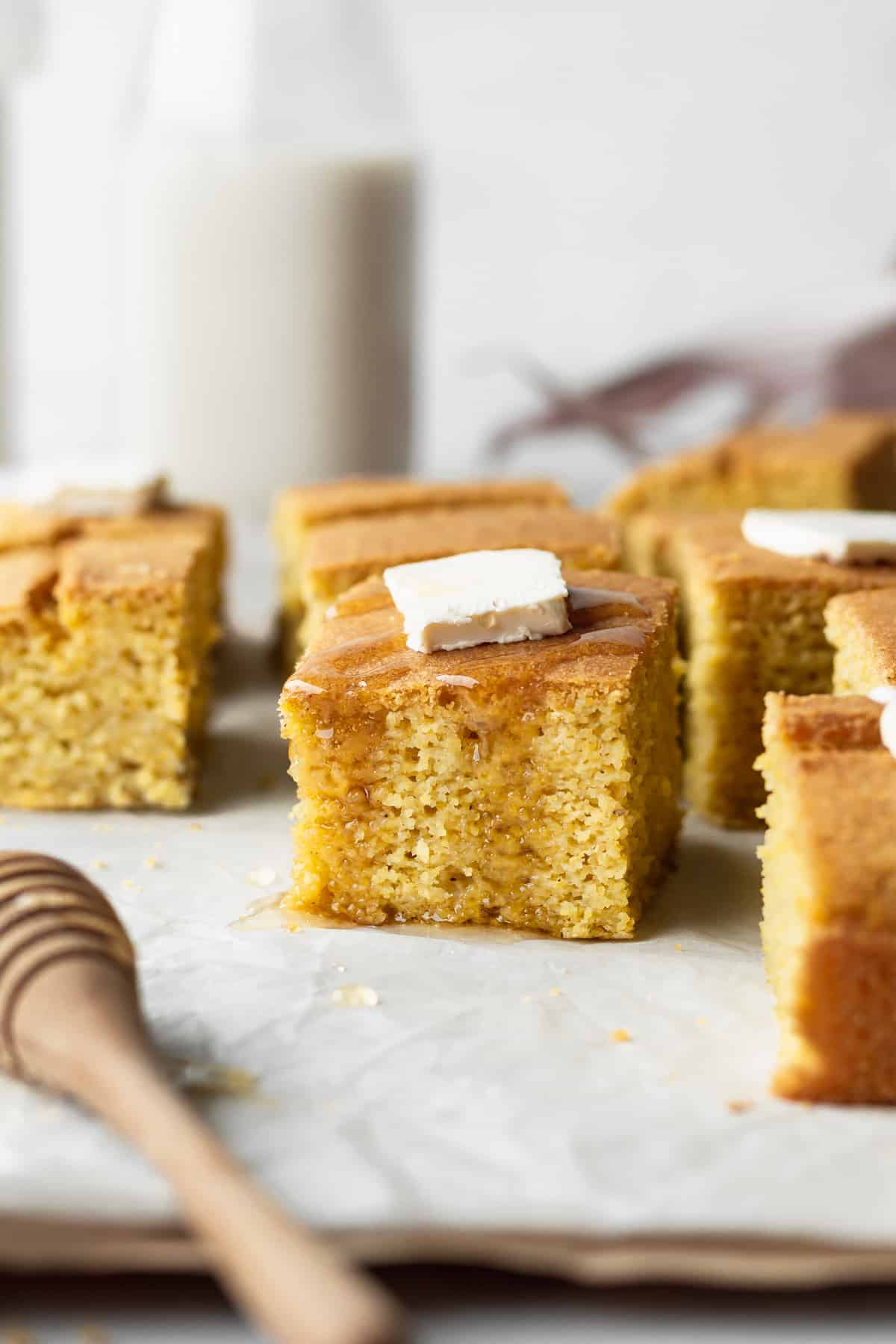 A square piece of gluten-free cornbread with a pad of butter and drizzle of honey.
