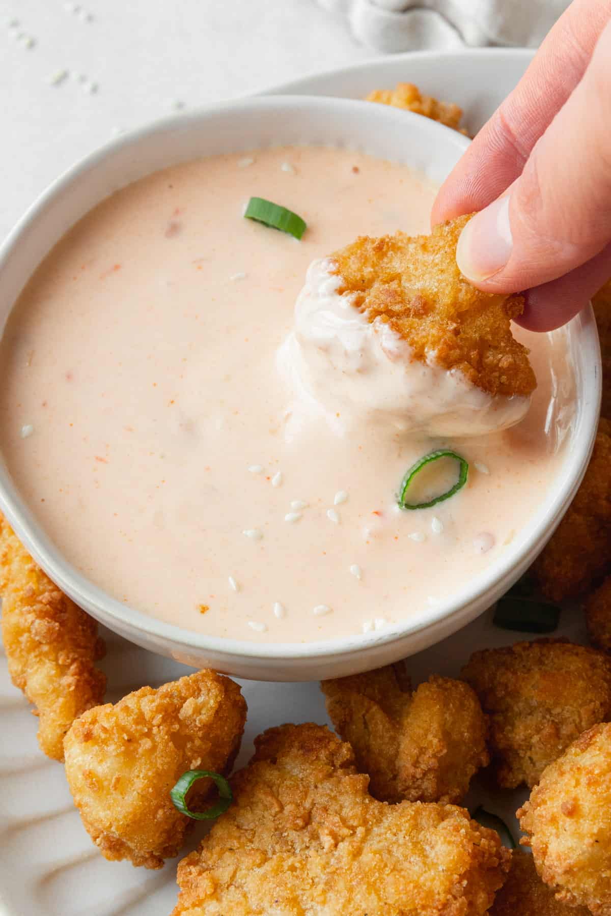 A hand holding a deep fried cauliflower and dipping it into a bowl of easy bang bang sauce.