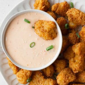 A deep fried cauliflower being dipped into a bowl of bang bang sauce.
