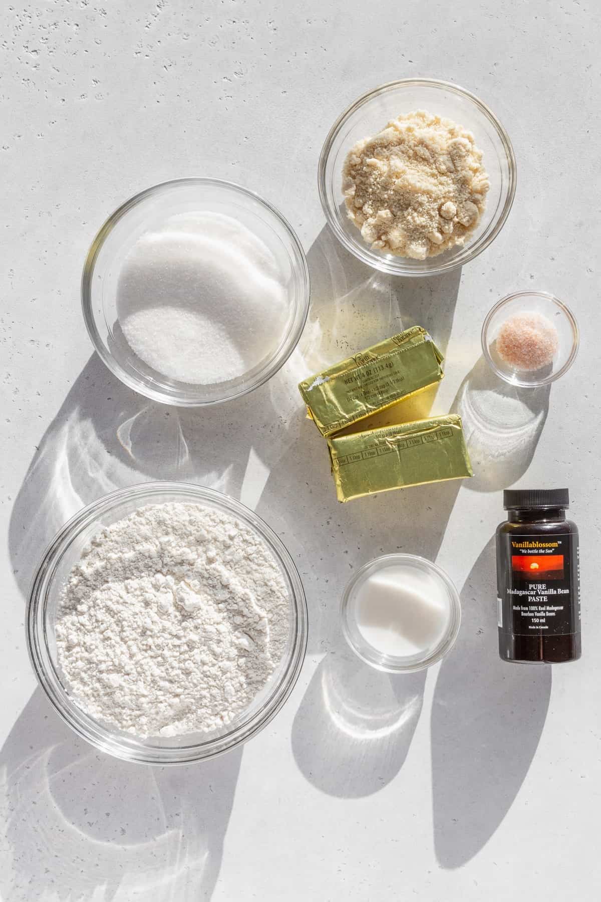 Ingredients for gluten free sugar cookies measured out into bowls on a white surface.