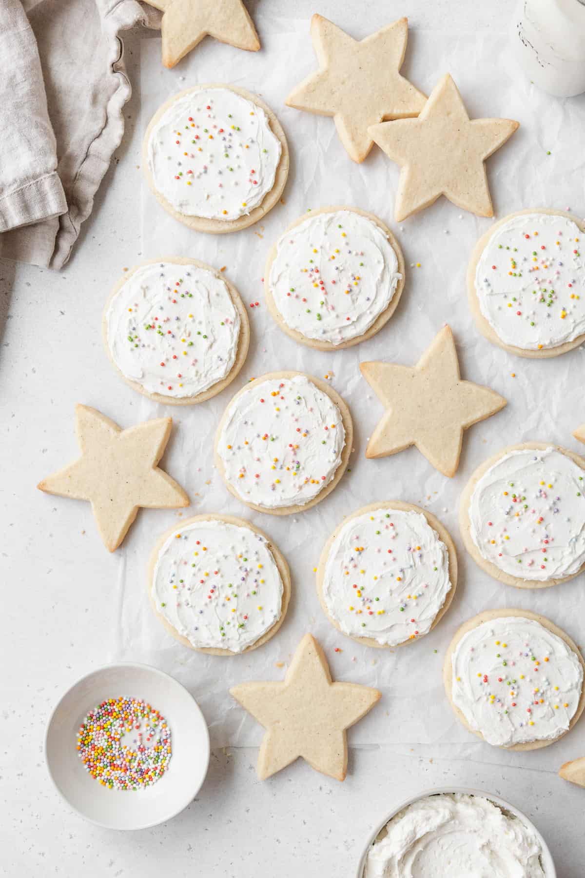 Star shaped sugar cookies and round frosted gluten free cookies laid out on a white surface.