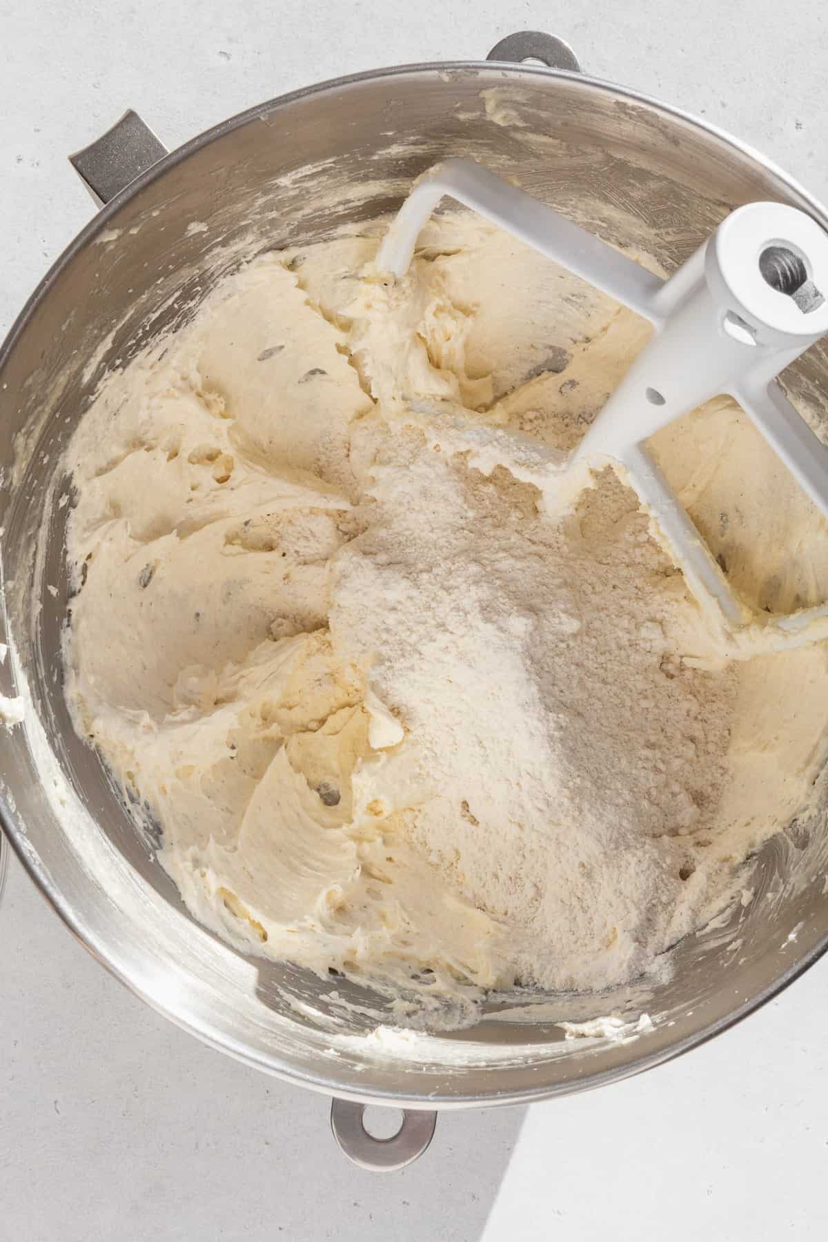 Dry ingredients added to the wet ingredients for sugar cookies in a metal bowl.
