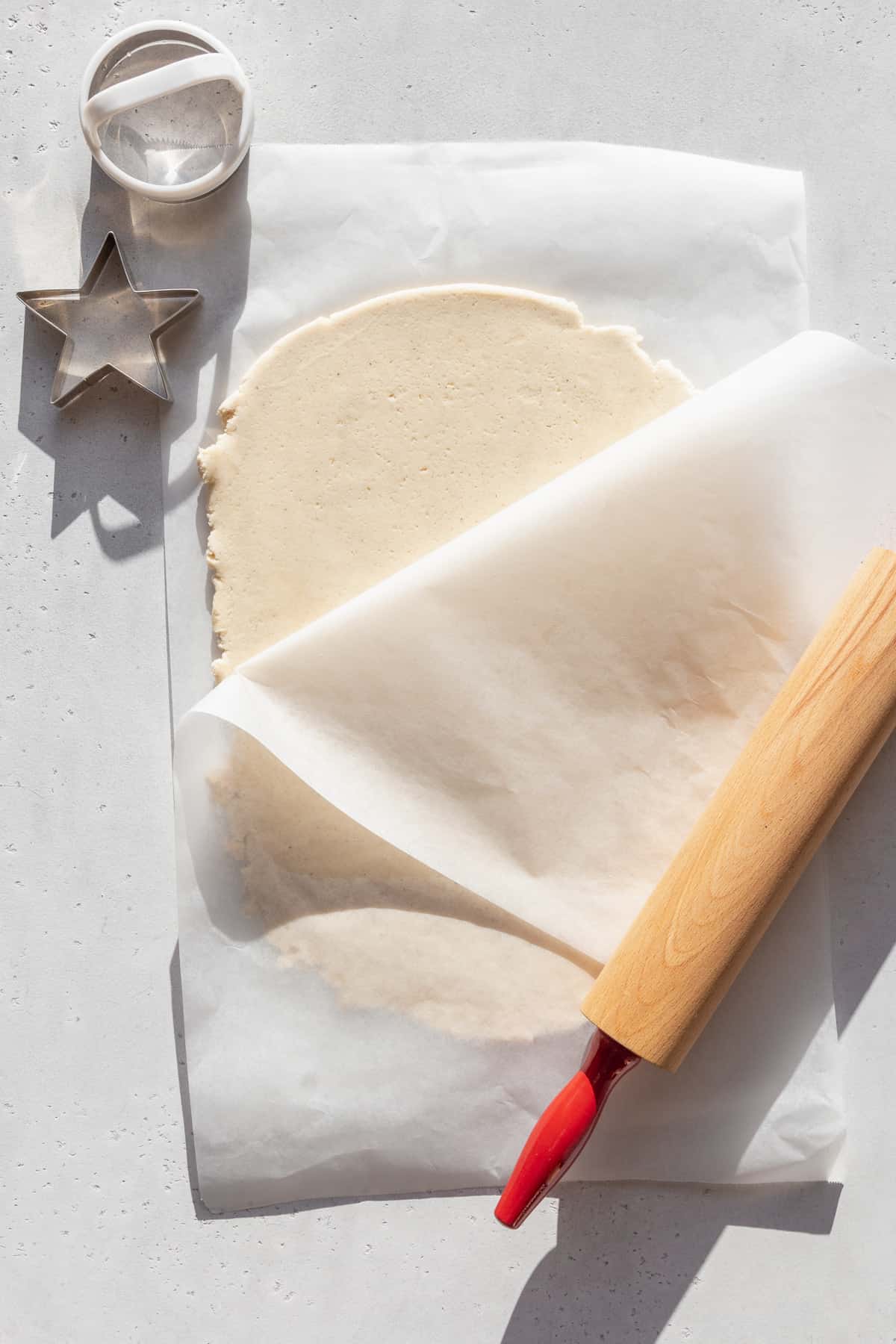 Gluten free sugar cookie dough rolled out between two sheets of parchment paper.