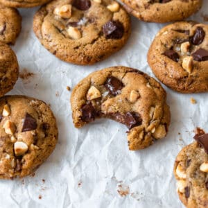 A bitten brown butter chocolate chip cookie surrounded by more cookies.