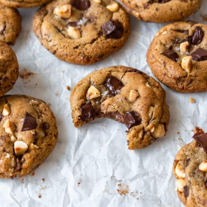 A bitten brown butter chocolate chip cookie surrounded by more cookies.