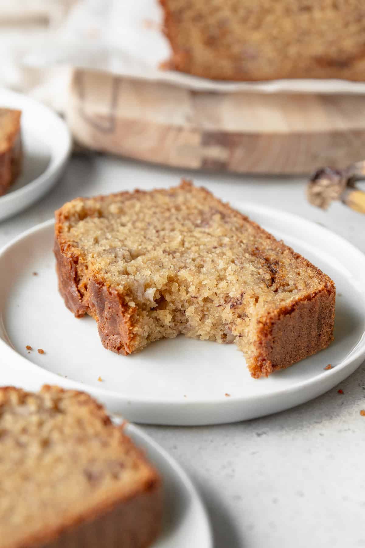 A bitten slice of gluten free banana bread on a small white plate.