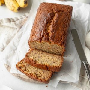 A sliced loaf of gluten free banana bread on sheets of parchment paper and a knife laying next to it.