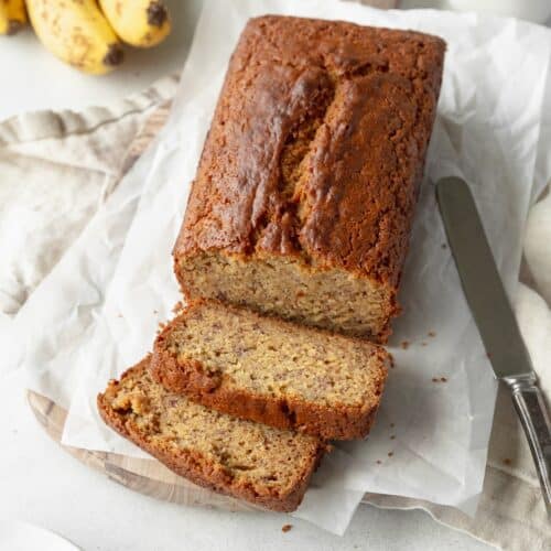 A sliced loaf of gluten free banana bread on sheets of parchment paper and a knife laying next to it.