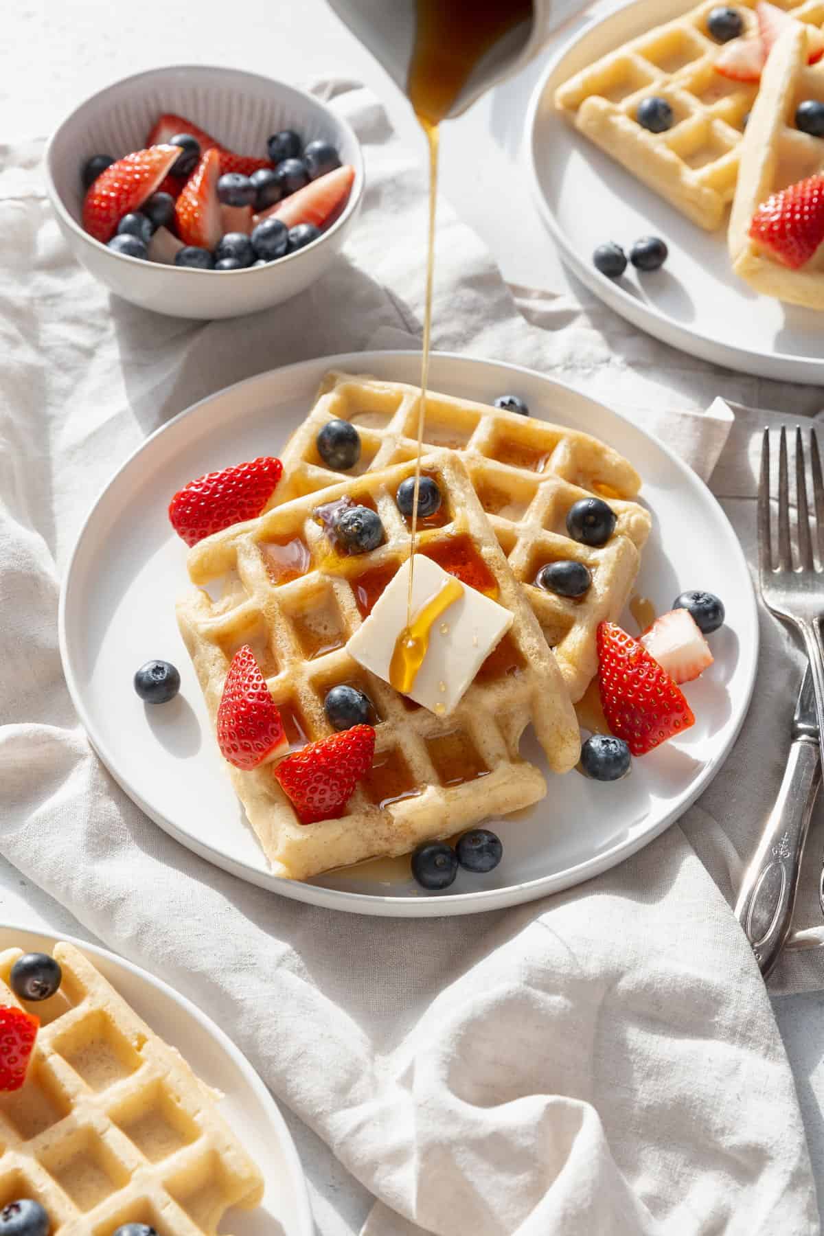 Two gluten-free waffles with fresh berries being drizzled with maple syrup.