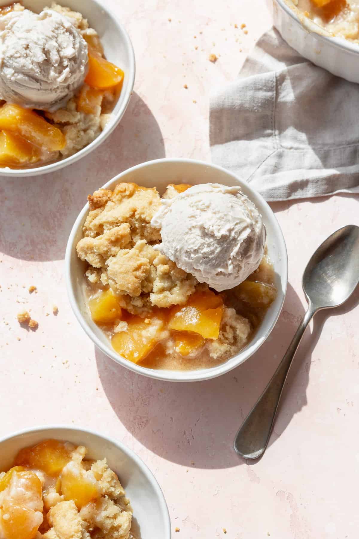 Overhead shot of peach cobbler with canned peaches in three white bowls with scoops of vanilla ice cream.