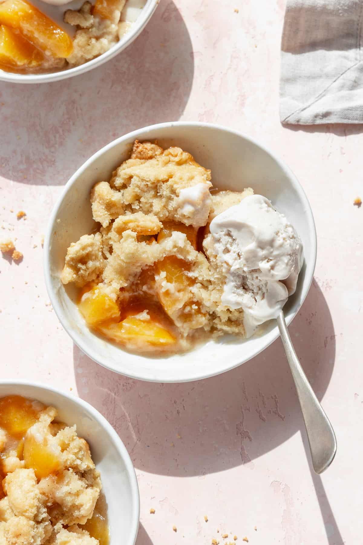 A half eaten bowl of peach cobbler with vanilla ice cream with a spoon in the bowl.