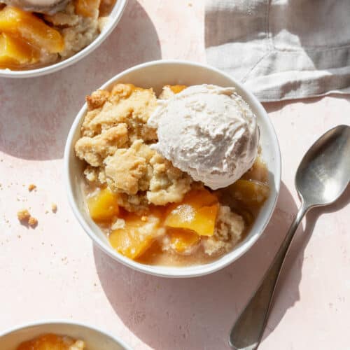 A bowl of peach cobbler with canned peaches and a scoop of vanilla ice cream.