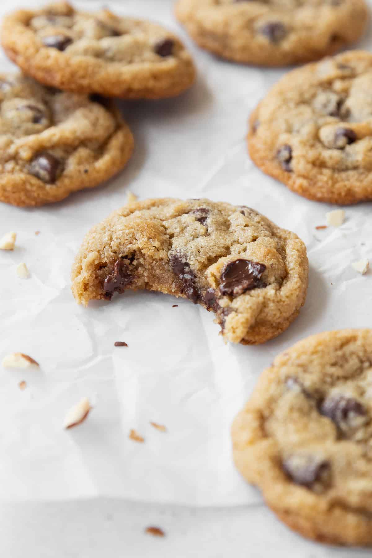 A bitten almond flour chocolate chip cookie on a white surface surrounded by more cookies.
