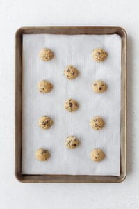 Cookie dough balls laid out on a parchment paper lined baking sheet.