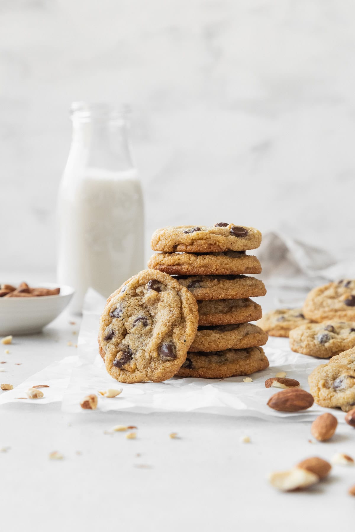 A stack of almond flour chocolate chip cookies on a piece of parchment paper with a bottle of milk in the background.