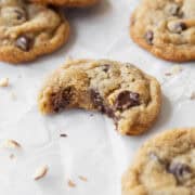 A square image of a bitten almond flour chocolate chip cookie on a white surface surrounded by more cookies.