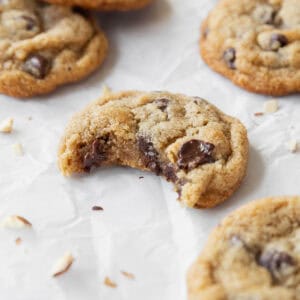 A square image of a bitten almond flour chocolate chip cookie on a white surface surrounded by more cookies.