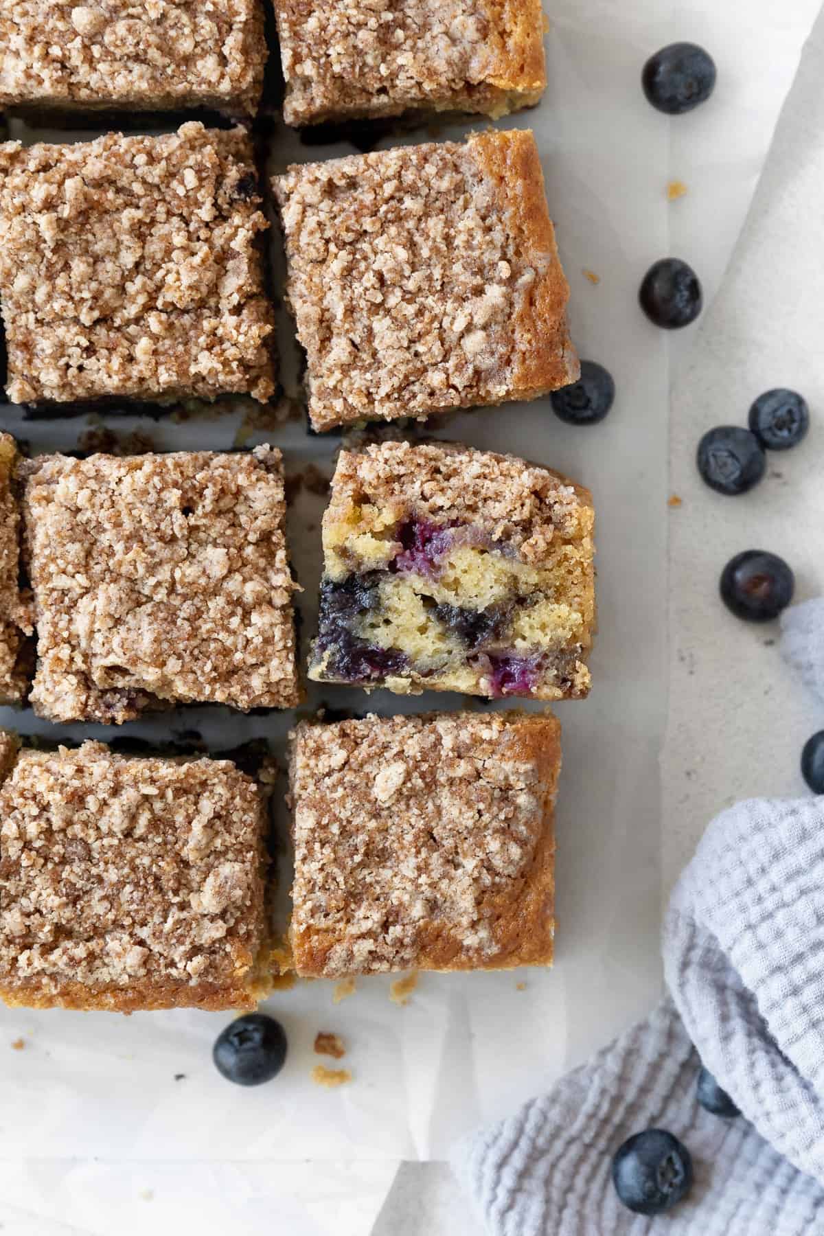 Overhead shot of blueberry coffee cake squares on parchment paper, with one tilted to show the inside of the cake.
