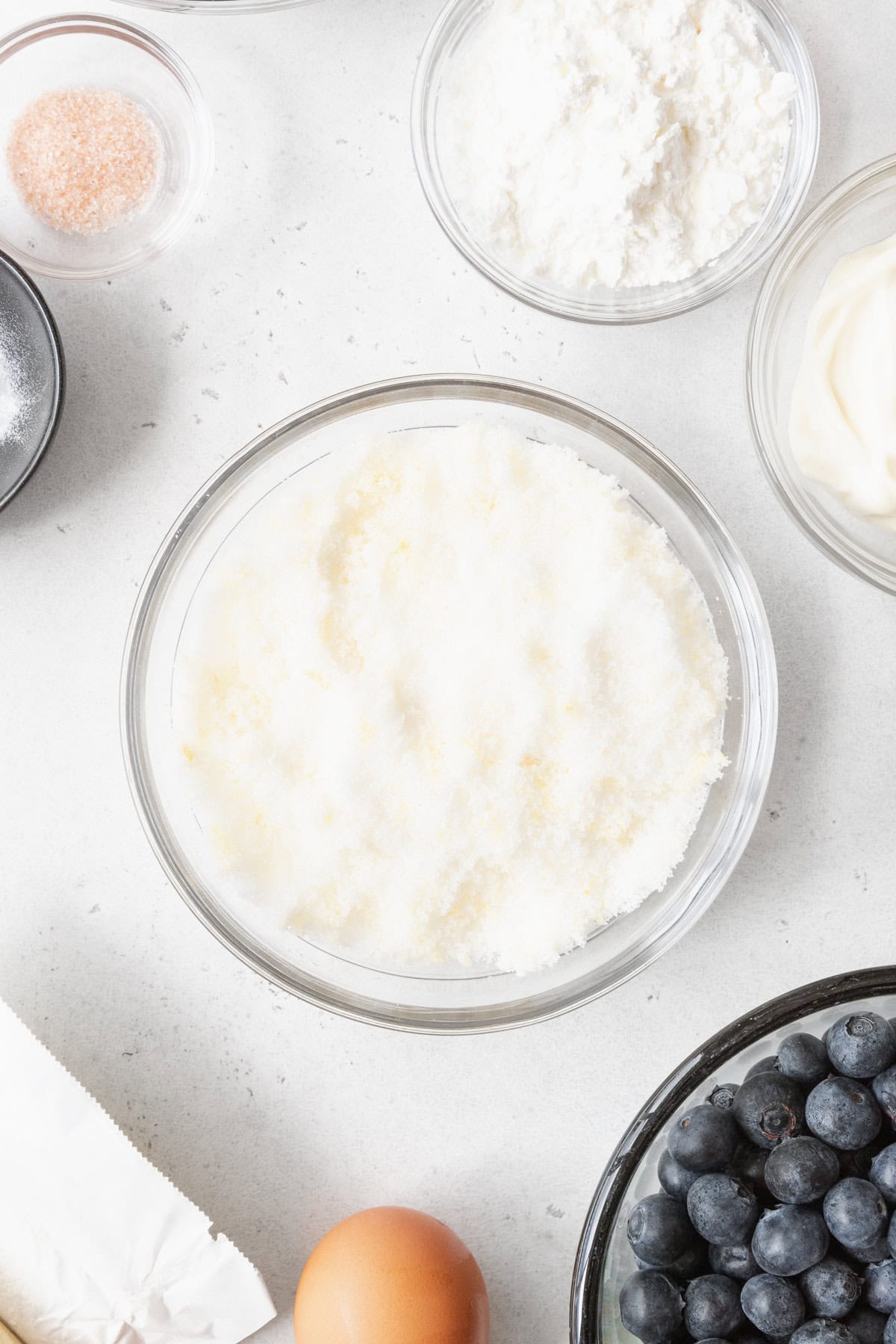 Lemon sugar in a glass bowl, surrounded by more bowls with bake ingredients.
