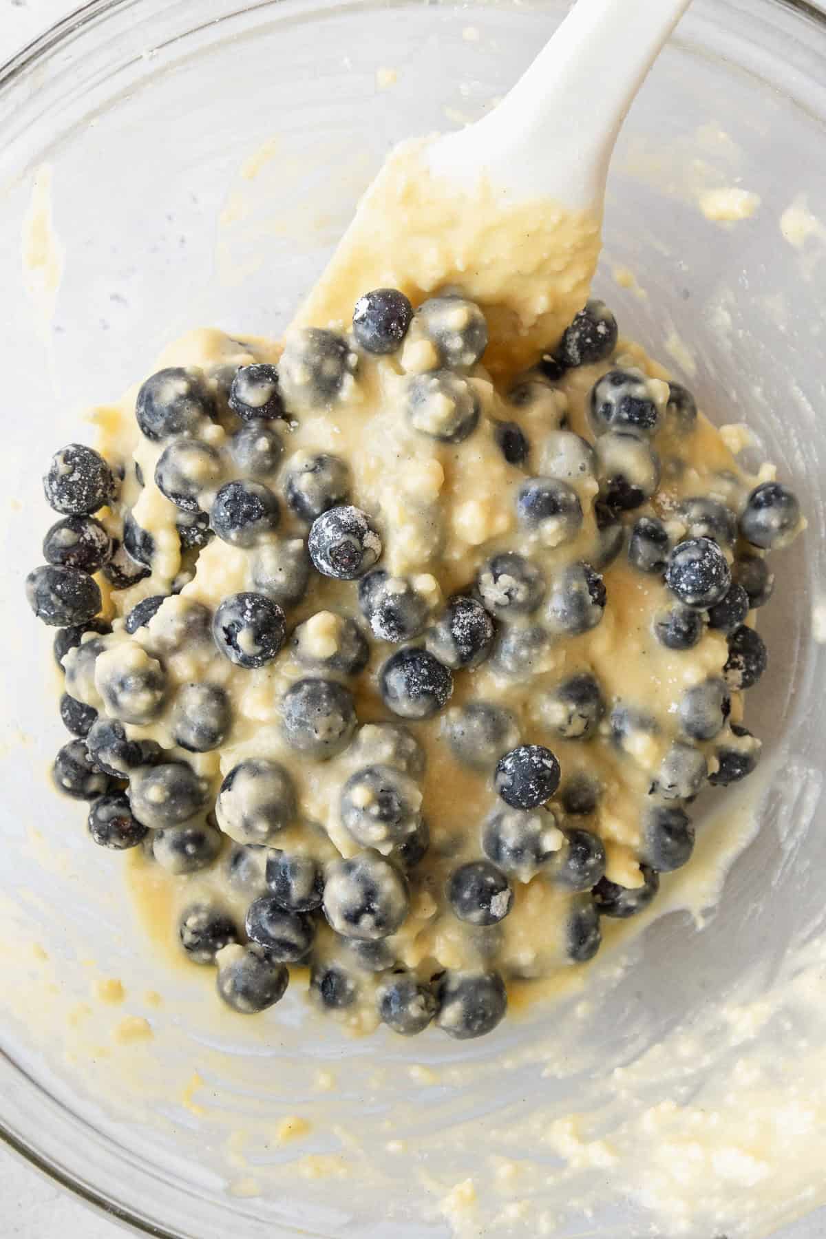 Blueberries being folded into cake batter with a white spatula.