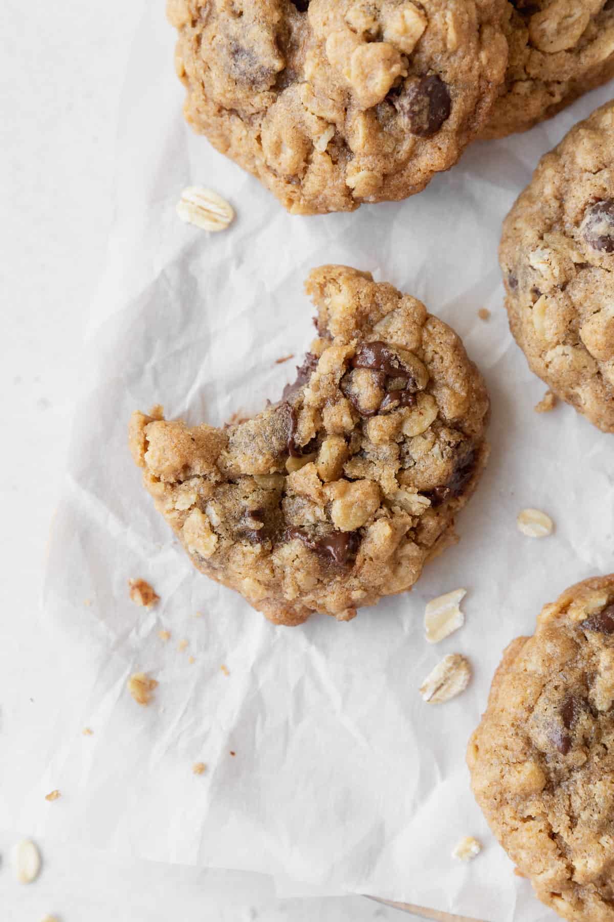 A bitten gluten free oatmeal cookie on a piece of parchment paper with more cookies and oats scattered around.