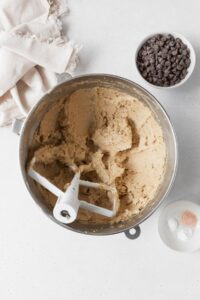 Wet ingredients for gluten free cookies in a metallic bowl with a bowl of chocolate chips beside it.