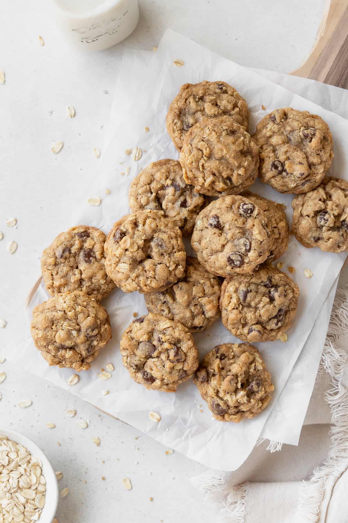 Gluten free oatmeal cookies on a parchment paper with oats scattered around.