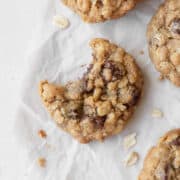 A bitten gluten-free oatmeal cookie with chocolate chips on a white surface surrounded by more cookies.