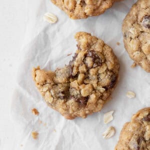 A bitten gluten-free oatmeal cookie with chocolate chips on a white surface surrounded by more cookies.