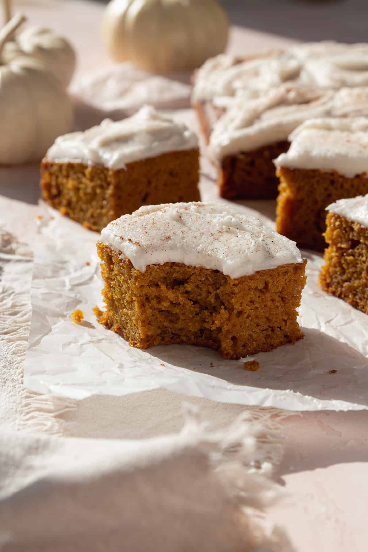 A bitten pumpkin bar topped with white frosting, with more slices behind.