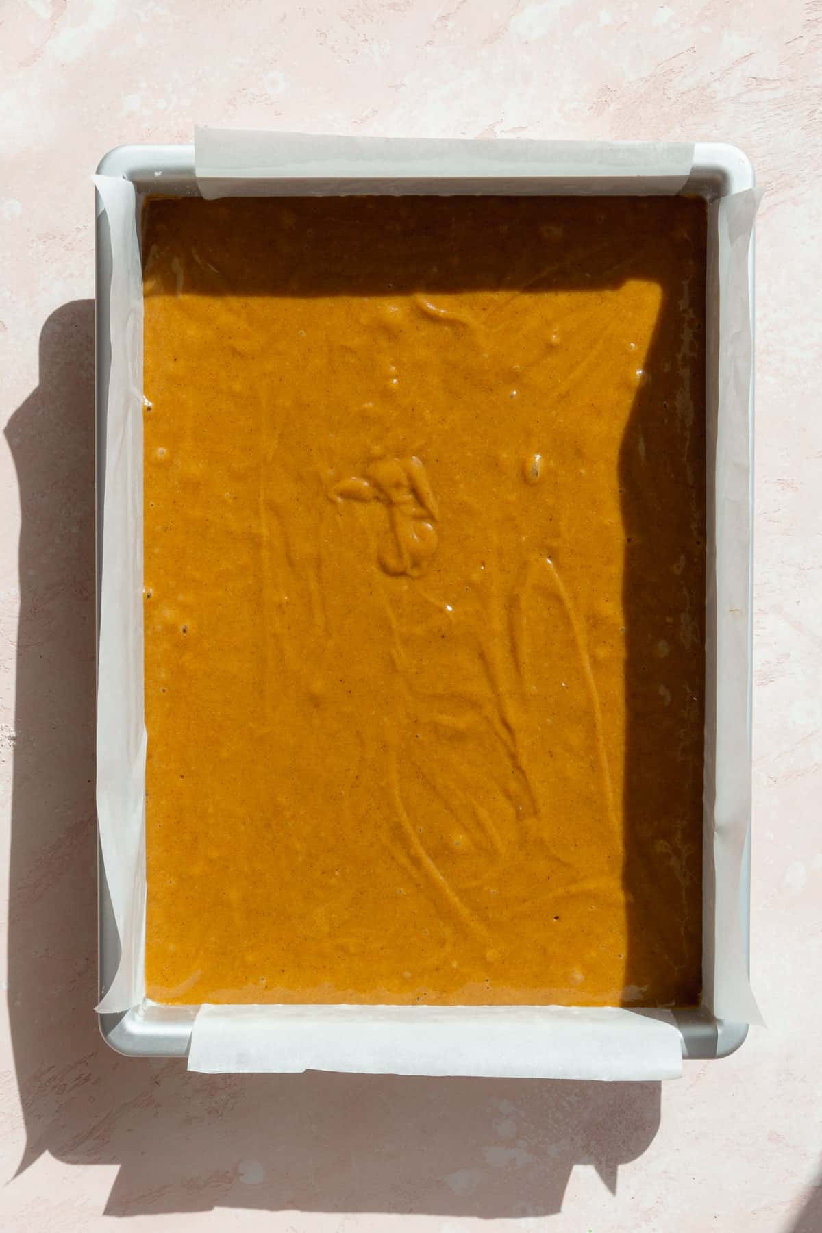 Pumpkin bars batter in a baking pan lined with parchment paper.