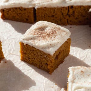 A pumpkin bar with cream cheese frosting, dusted with cinnamon on top.