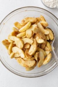 Sliced apples tossed with spices in a glass bowl.