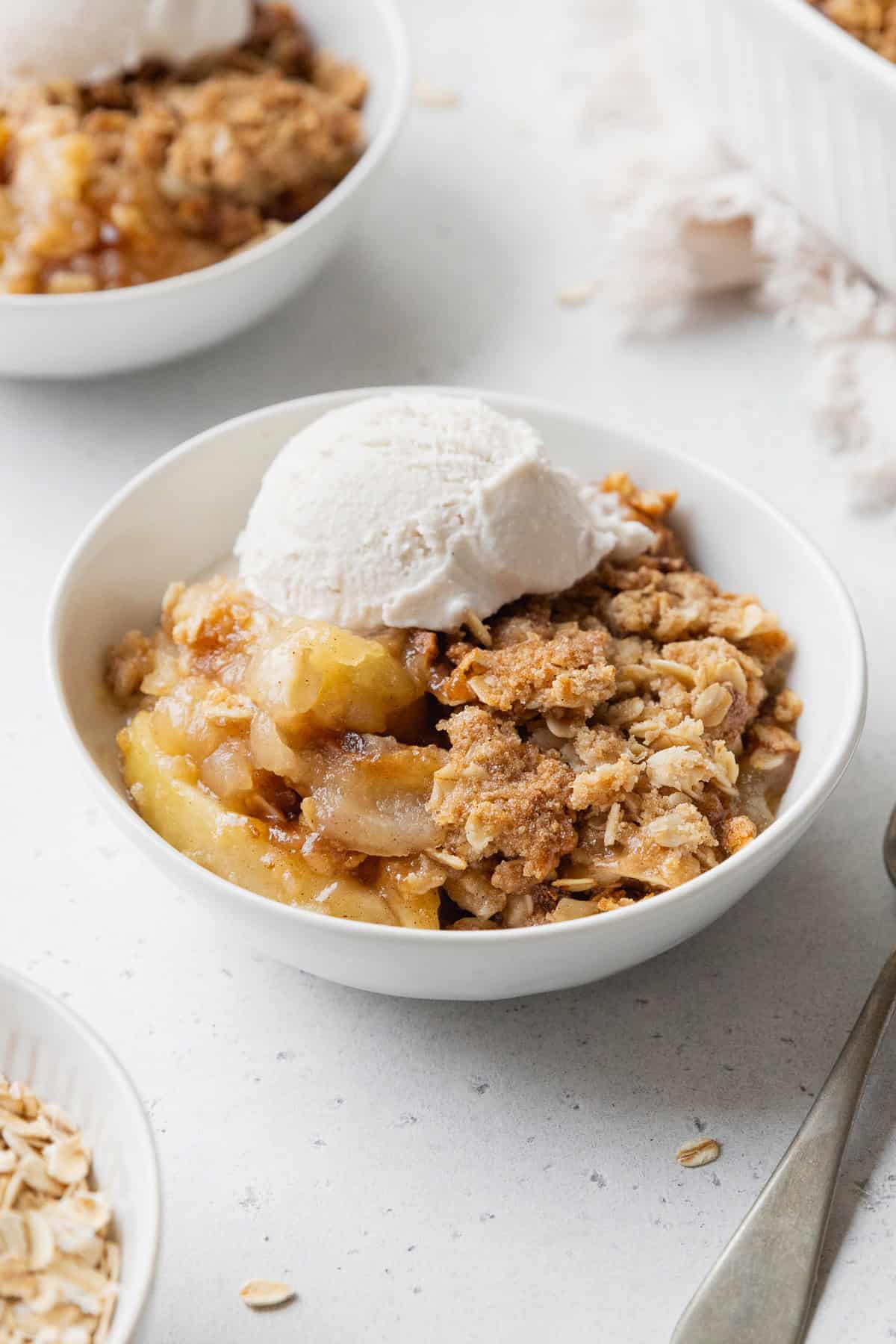 Apple crisp in a white bowl with a scoop on vanilla ice cream on top.