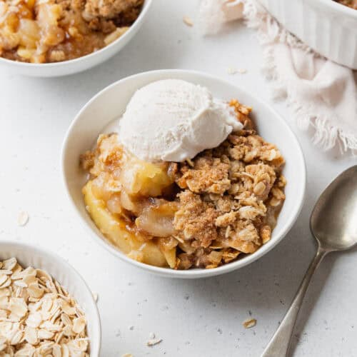 A bowl of gluten free apple crisp with a scoop of vanilla ice cream on top.
