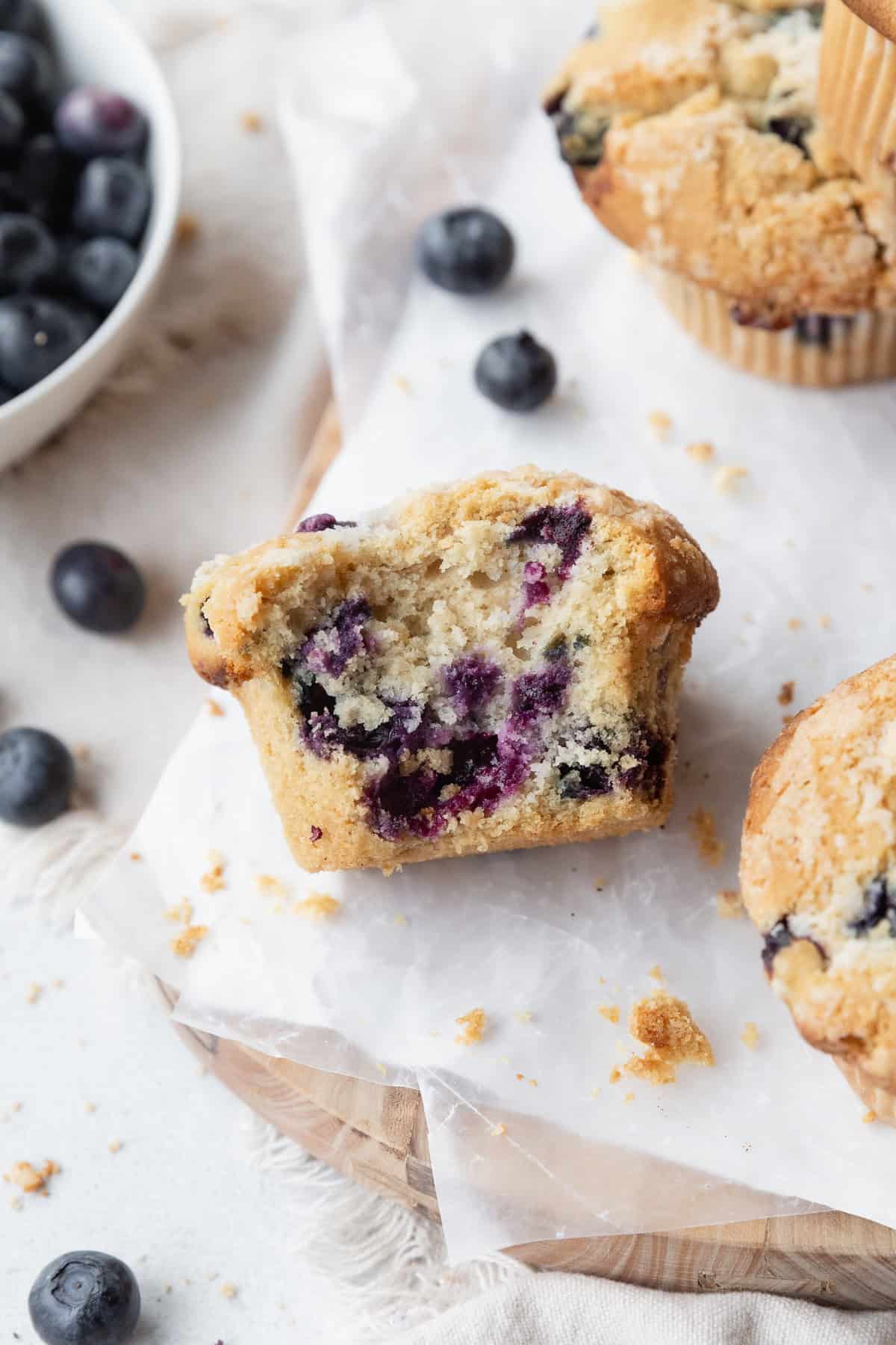 A bitten blueberry muffin on its side, showing specks of juicy blueberries inside.