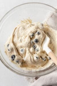 Blueberries being folded into muffin batter in a glass bowl.