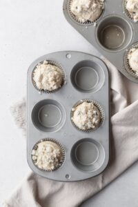 Muffin tins with blueberry muffin batter in every other muffin cup.