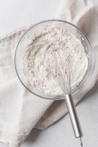 A glass bowl of dry ingredients with a whisk.
