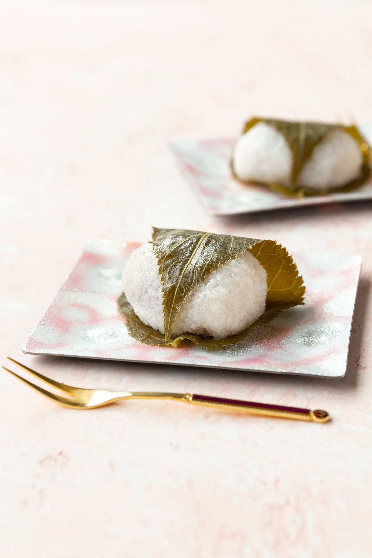 Sakura mochi on a pink dessert plate on a pink surface.