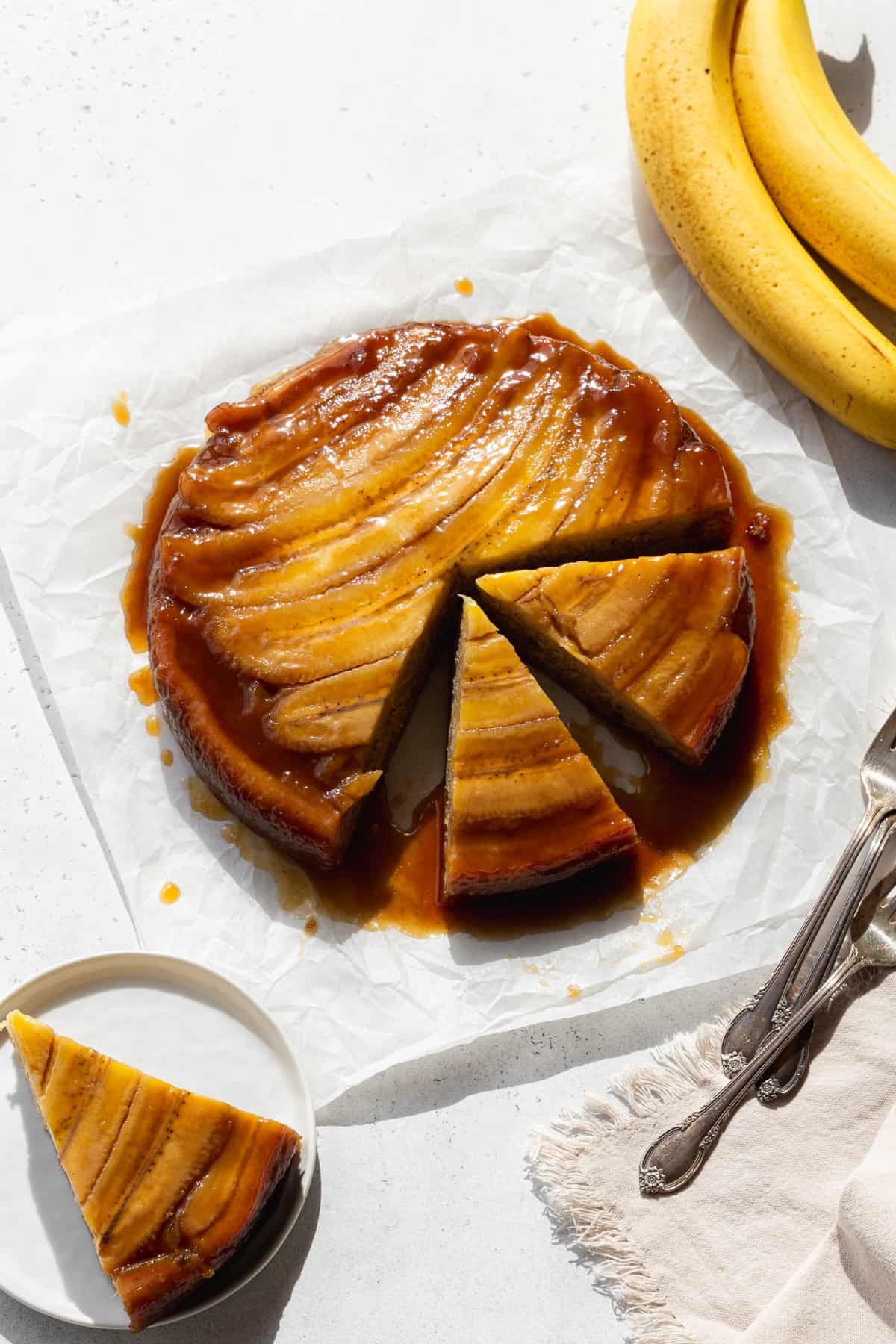 A banana upside down cake with two slices cut out, and another slice on a small dessert plate.