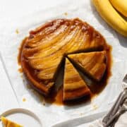 A banana upside down cake on parchment paper with two slices cut out.