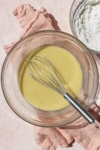 A glass bowl with the wet ingredients of waffle batter being whisked together.