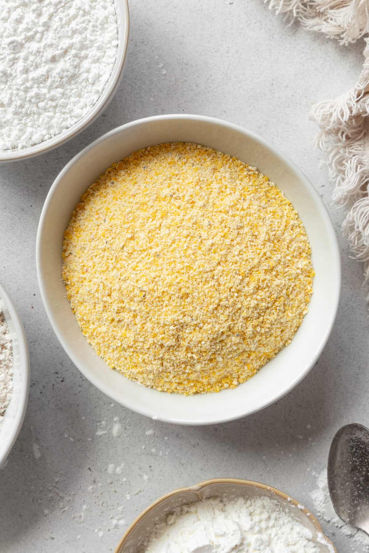 A bowl of cornmeal with bowls of other flours around it.