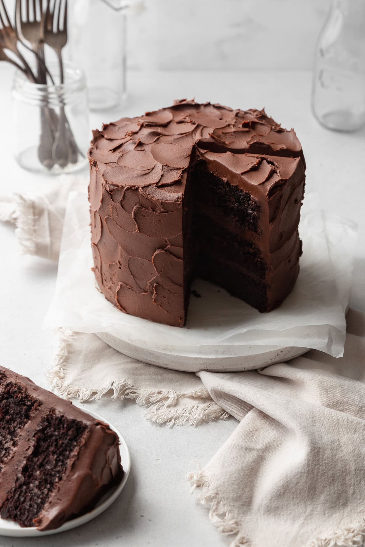 A frosted chocolate cake with a slice cut out, and another slice on a plate in front.