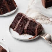 A bitten slice of gluten free chocolate cake with chocolate frosting on a small white plate.