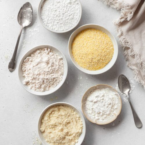 Bowls of different gluten free flours on a light grey surface with two spoons.